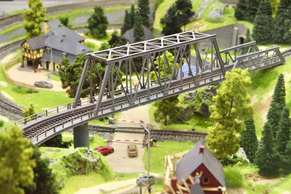 Detailed miniature diorama featuring a railway bridge, lush greenery, and model structures.